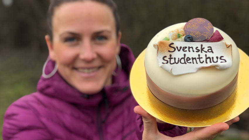 Kvinna i lila jacka håller tårta med texten "Svenska Studenthus".